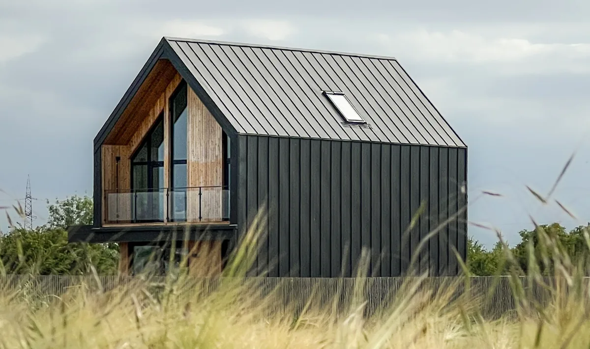 A contemporary dark-clad home with a gabled metal roof standing alone in a grassy rural field